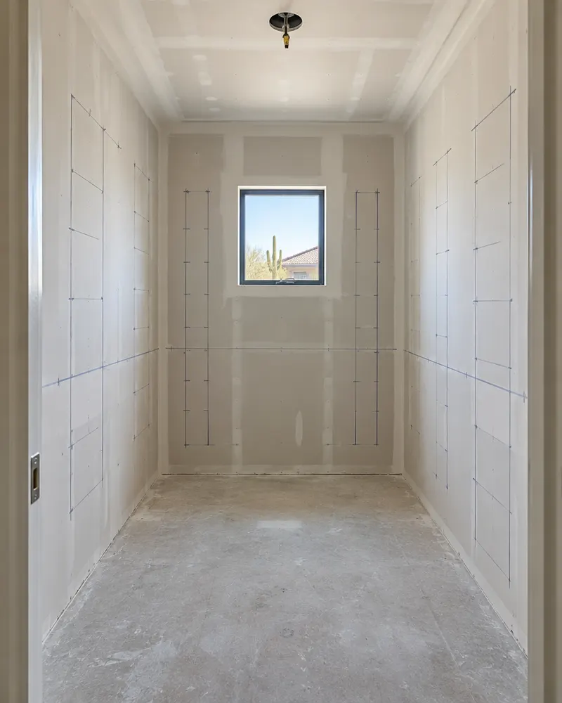 Empty walk-in closet stripped to bare drywall before a custom install, marks on the wall for panel positions, new lighting box in the ceiling
